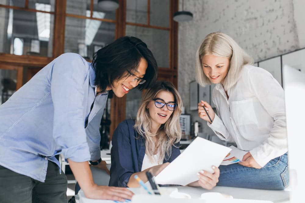 beautiful blonde girl glasses showing report asian colleague which standing beside her table 1 2 Clases de alemán online